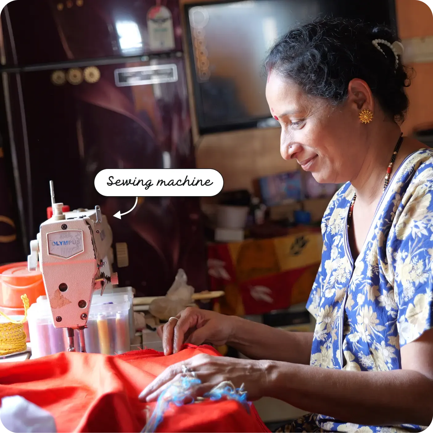 A smiling woman guides fabric under the needle of a sewing machine, with spools of thread nearby. A label points to the machine as a "Sewing machine".
