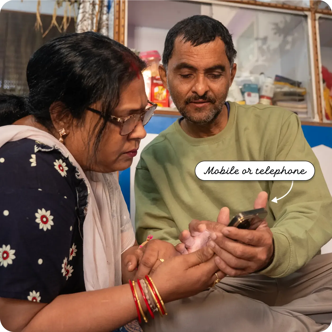 A man and woman sitting closely together, both focused on a smartphone. A label points to the device as a "Mobile or telephone".